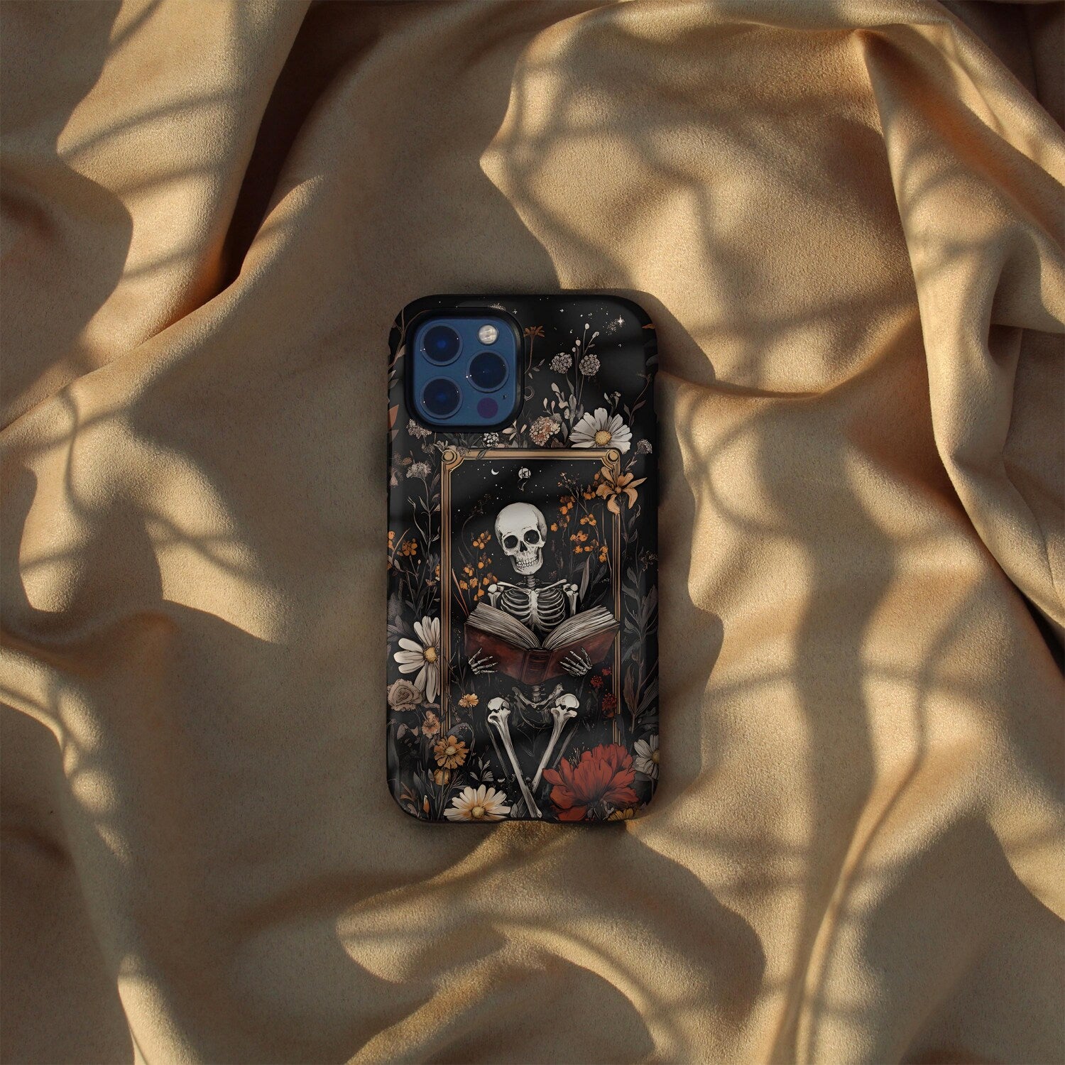 Phone case with skeleton and floral design on a beige fabric background